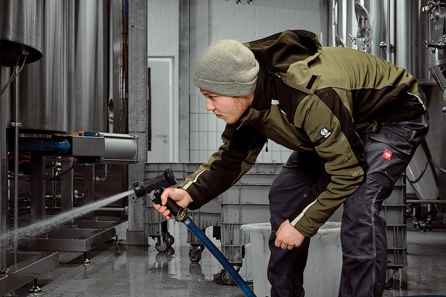 Mitarbeiter reinigt eine Anlage in der Produktionshalle mit dem Wasserschlauch