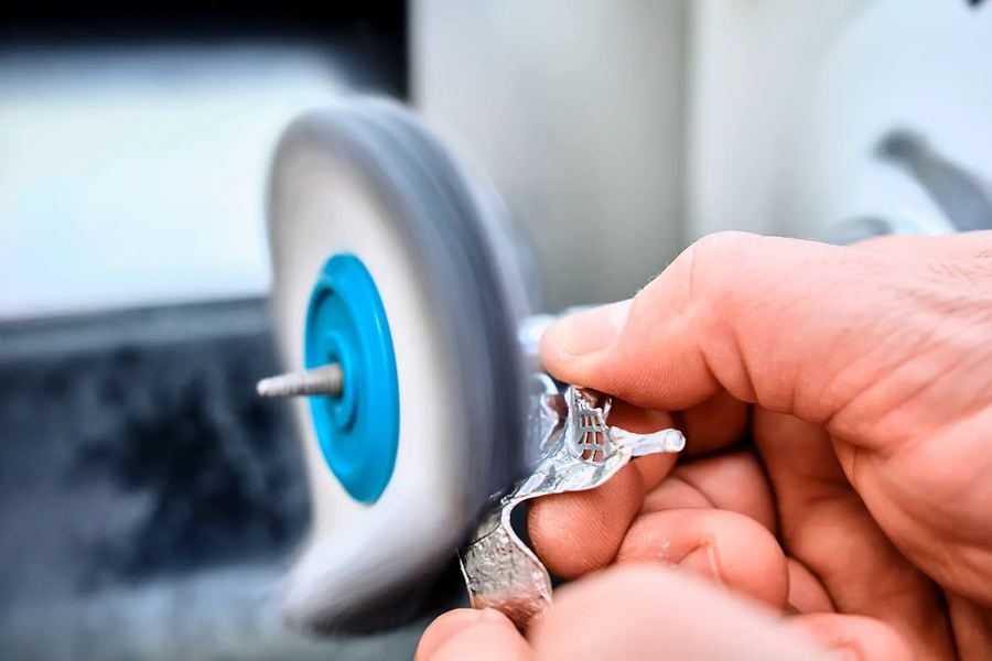 Metallteil wird an einer Polierscheibe von Hand nachbearbeitet