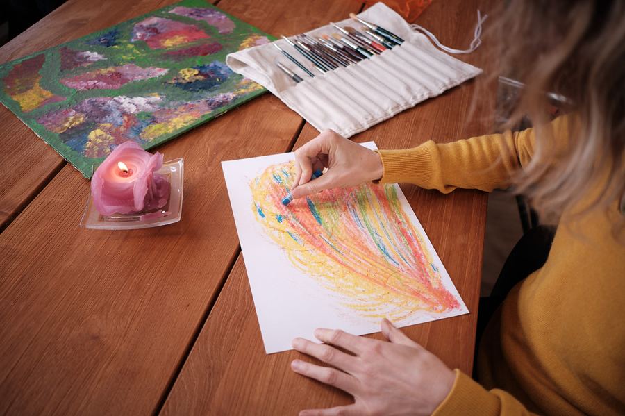 Hand zeichnet mit Pastellkreide ein farbiges Bild an einem Holztisch
