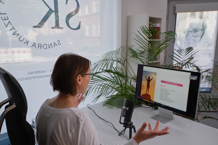Frau im Video-Call vor Monitor und Mikrofon in ihrem Büro